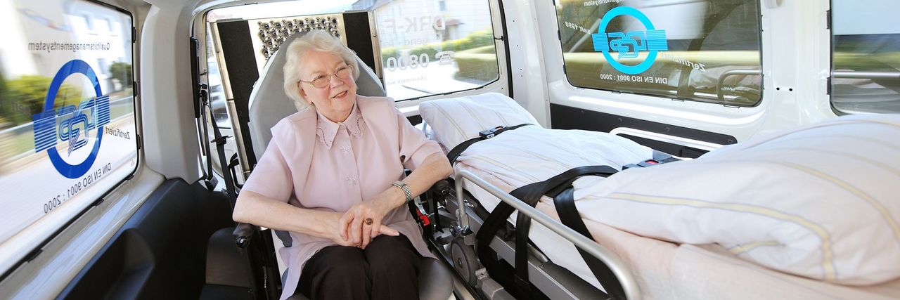 Portrait einer lächelnden Seniorin in einem Fahrzeug des DRK Krankentransportes.